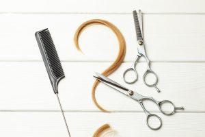 Question mark made of curl hair. Concept of how to choose a hairstyle or hairdresser. White wood background with hair and thinning scissors.